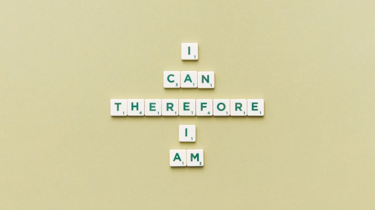 Inspirational phrase 'I Can Therefore I Am' arranged using Scrabble tiles on a green background.